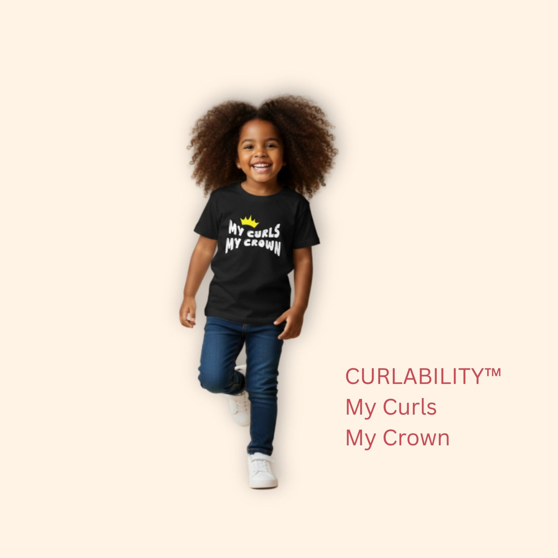 Smiling curly-haired girl walking in a studio wearing a black “My Curls My Crown” t-shirt and jeans.