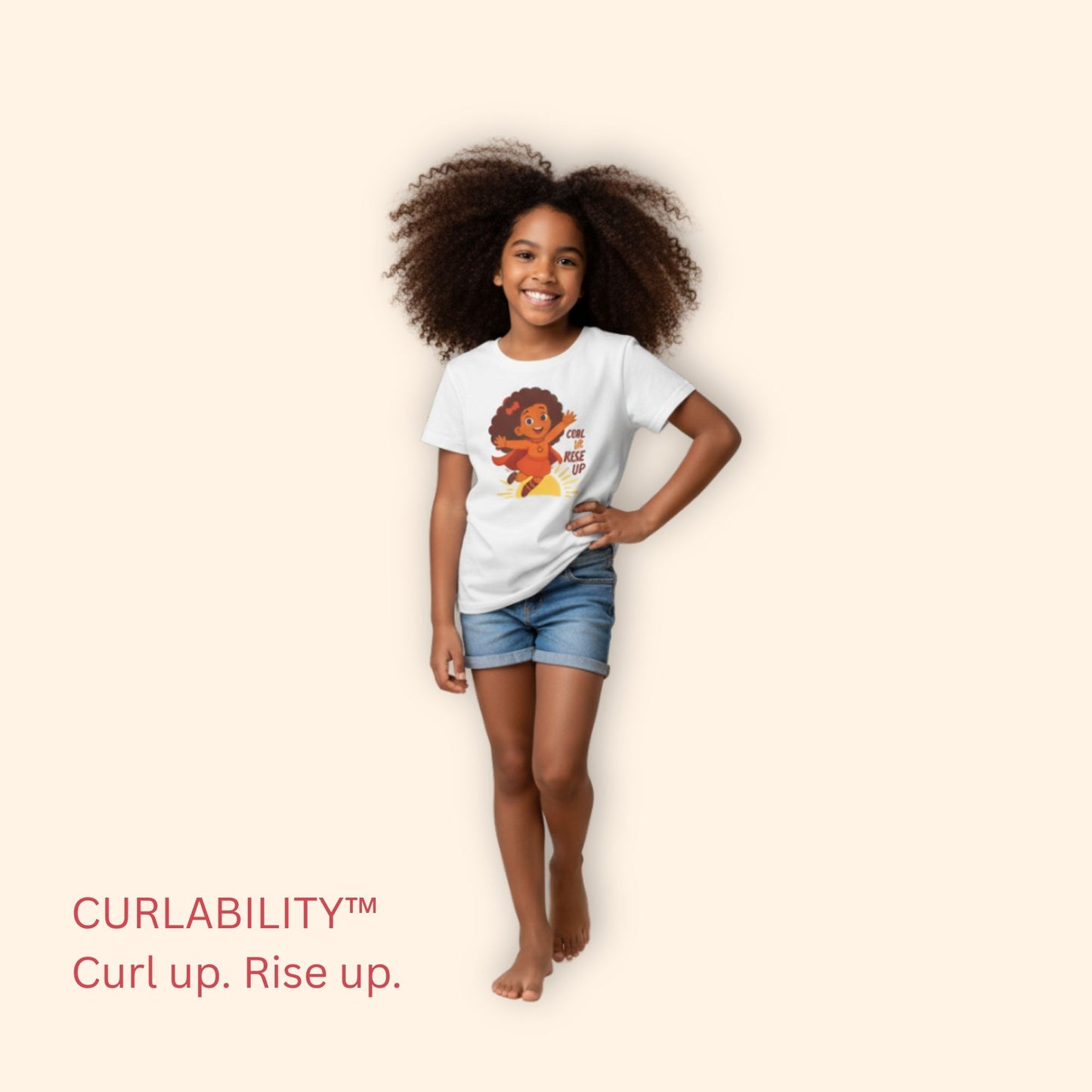 Smiling curly-haired girl standing in a studio wearing a white “Curl Up. Rise Up.” t-shirt and denim shorts.