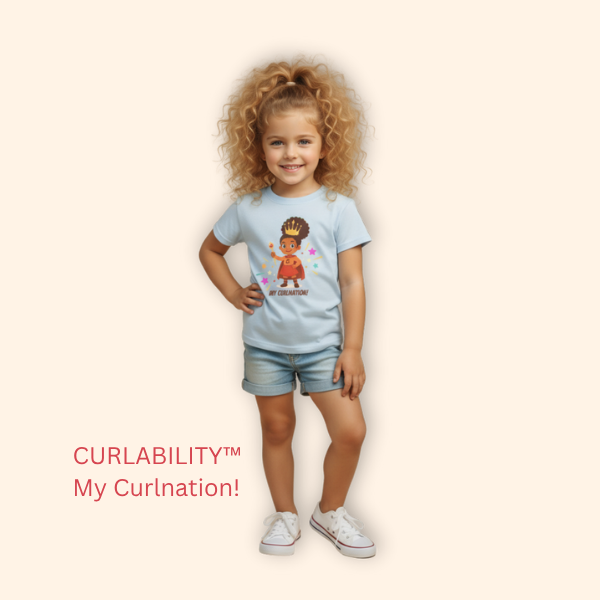 Smiling curly-haired girl standing in a studio wearing a light blue “My Curlination!” t-shirt and denim shorts.
