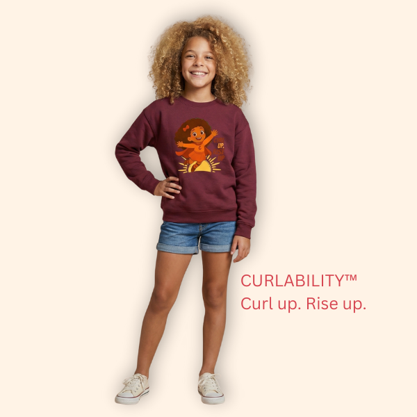 Studio photo of a young girl wearing a maroon “Curl Up. Rise Up.” kids’ sweatshirt, standing against a neutral background.