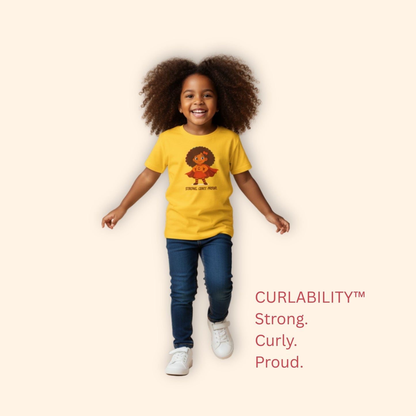 Smiling curly-haired girl running in a studio wearing a yellow “Strong. Curly. Proud.” t-shirt.