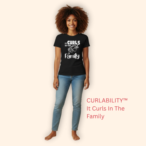 A smiling woman with curly hair wearing a black “It Curls In The Family” t-shirt from CURLABILITY™, standing casually against a neutral background.